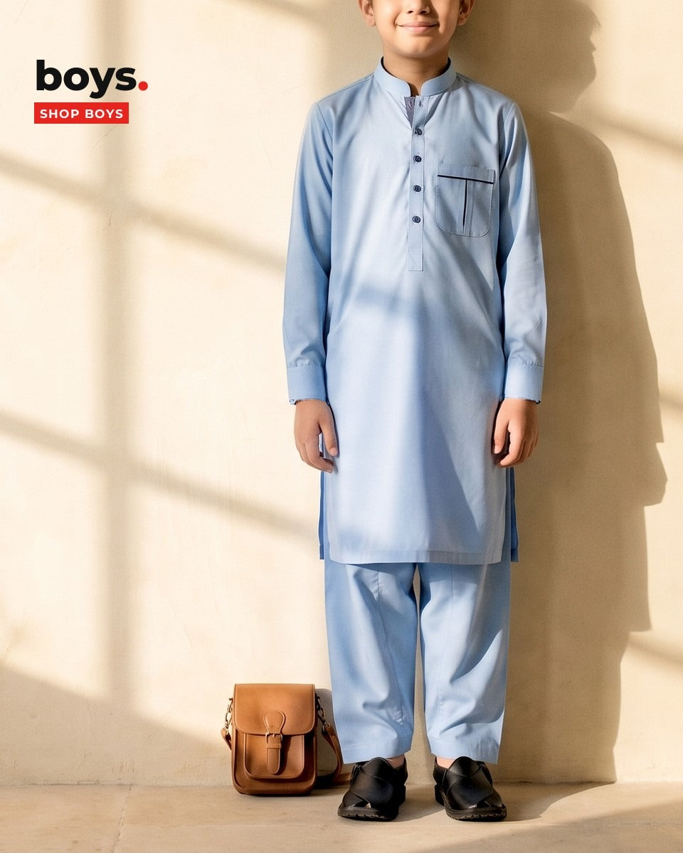 Boy in a sky blue cotton shalwar kameez against a sunlit limewash wall - Suhaib Gulzar boys' shalwar kameez